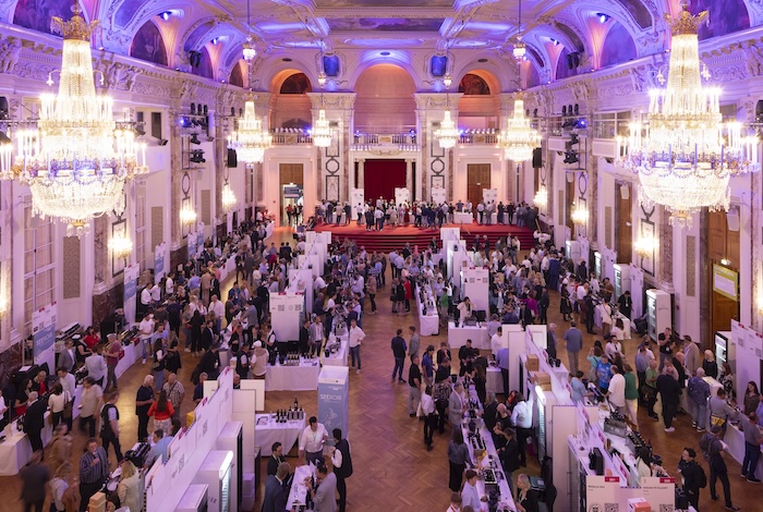 Großer Veranstaltungsraum mit vielen Ständen und Besuchern bei einer Weinmesse mit eleganter Beleuchtung.