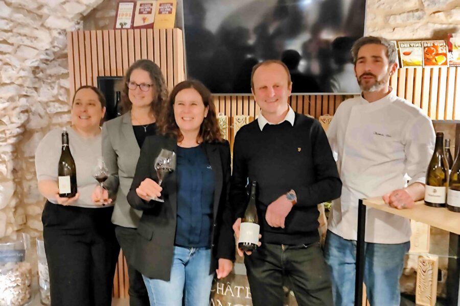 Fünf Personen stehen zusammen in einem Weinkeller, jede mit einem Glas Wein in der Hand, umgeben von Weinflaschen.