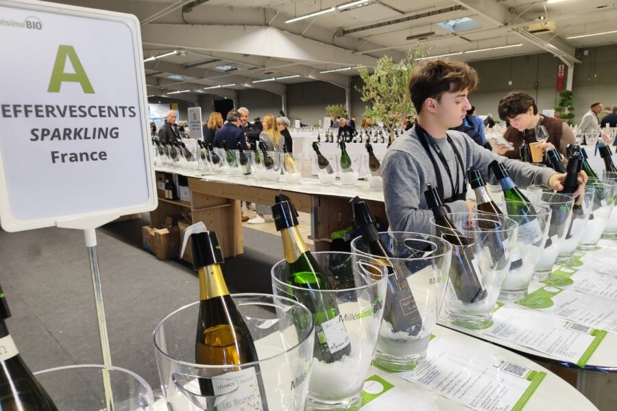 Ein junger Mann steht an einem Tisch mit verschiedenen Flaschen Sekt und Schaumwein bei einer Veranstaltung in Frankreich.
