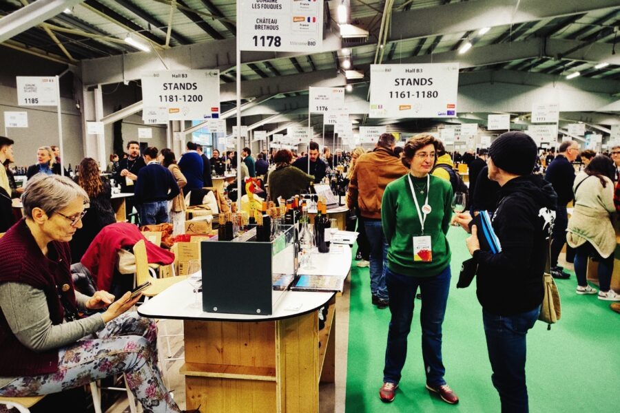 Menschen auf einer Weinmesse mit Ständen und Besuchern in einem großen Ausstellungsraum.